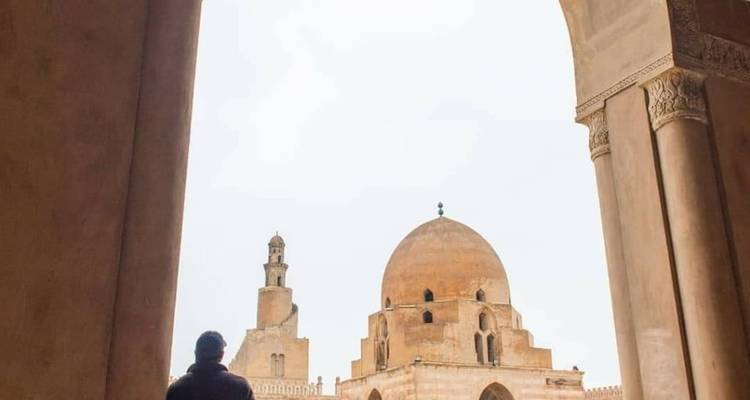 Person, die unter einem Torbogen steht, mit einer Moschee im Hintergrund.