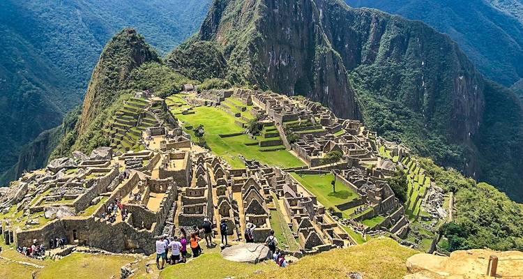 Panoramisch uitzicht op Machu Picchu met bezoekers die tussen de ruïnes wandelen.