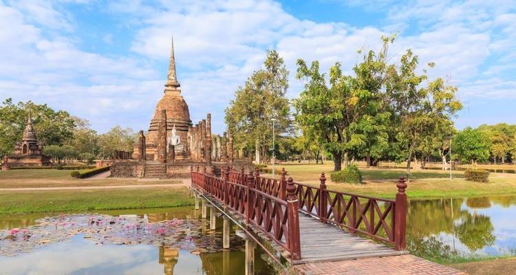 Historischer Tempel mit Turm, betrachtet von einer Holzbrücke über einen spiegelnden Teich.