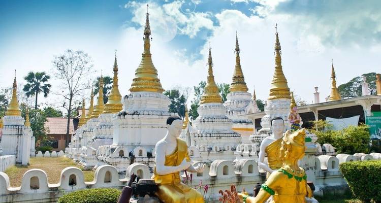 Weißer Tempel mit goldenen Türmen und Statuen in einem dekorativen Garten.