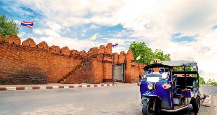 Traditionelles thailändisches Tuk-Tuk, das in der Nähe einer historischen Backsteinmauer mit Flaggen geparkt ist.