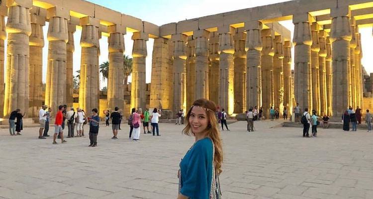 Frau in einem blauen Kleid vor beleuchteten antiken Säulen.