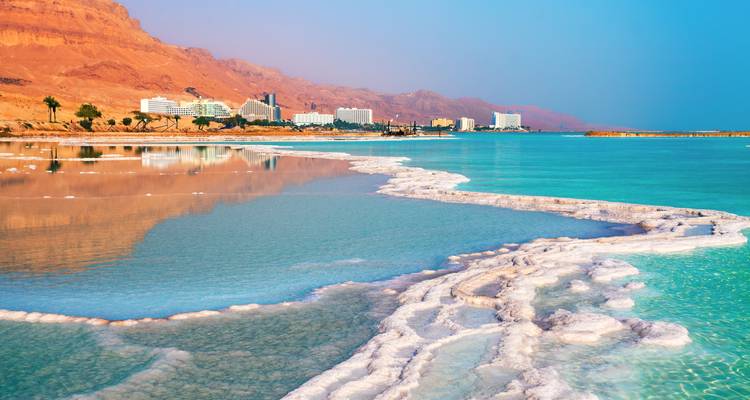 Salt formations and turquoise water with mountains in the background.