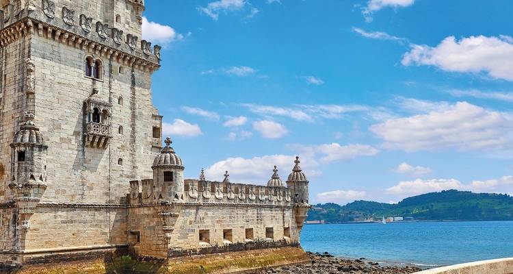 Historische stenen toren aan het water onder een heldere blauwe lucht.