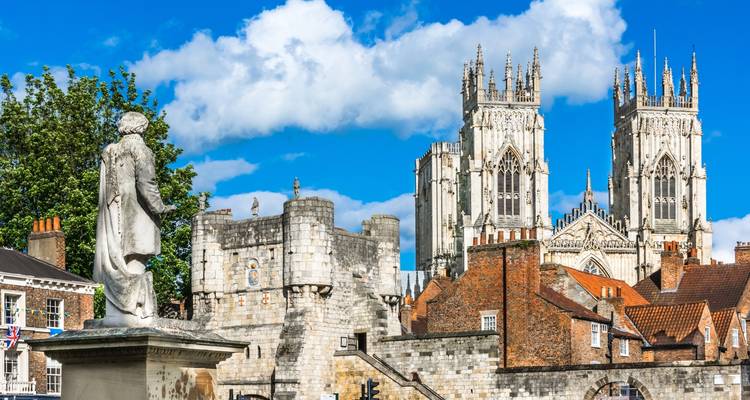 York Minster met standbeeld op de voorgrond onder een blauwe hemel.