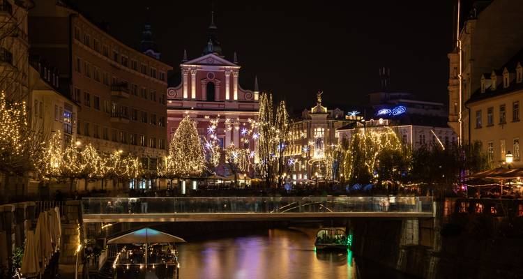 Nachtszene an einem Fluss mit Stadtgebäuden, die mit Lichtern geschmückt sind.