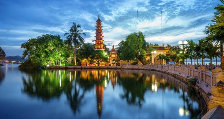 Temple by the lake with reflections and trees surrounding it at dusk.