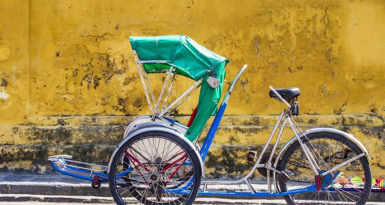 Rickshaw parked along a yellow, aged wall.