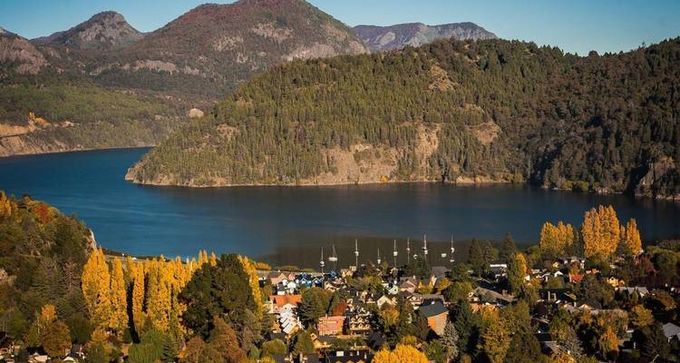 Een stad aan een meer met bomen in herfstkleuren en bergen.