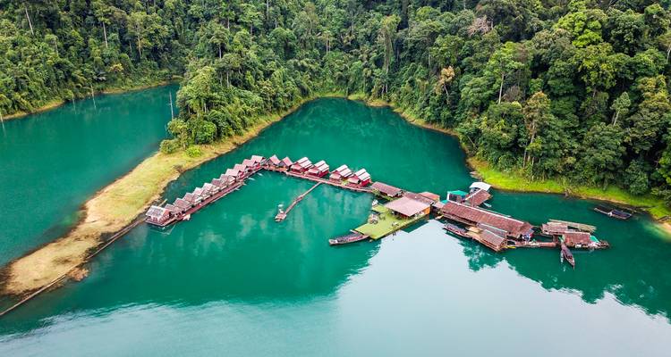 Aerial view of floating bungalow resort arranged on a turquoise lake fringed by dense rainforest.