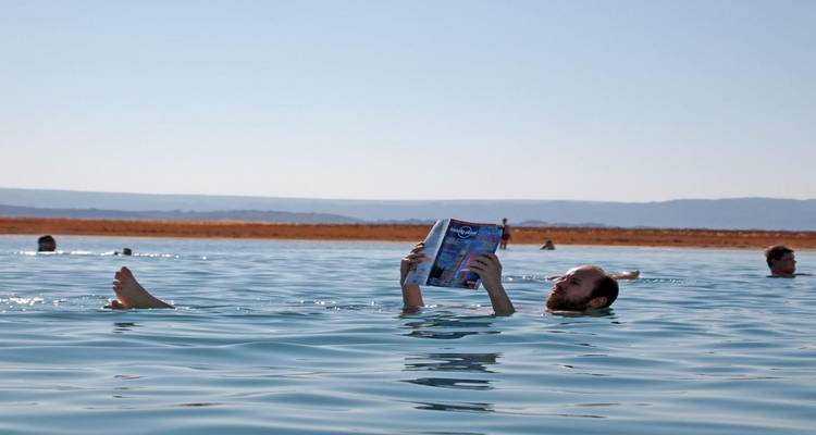 Persona flotando en el agua leyendo un libro con montañas de fondo.