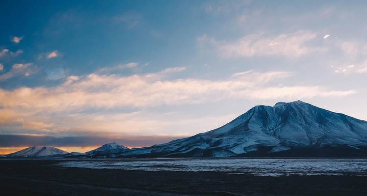 Paisaje montañoso con picos nevados y un cielo colorido.