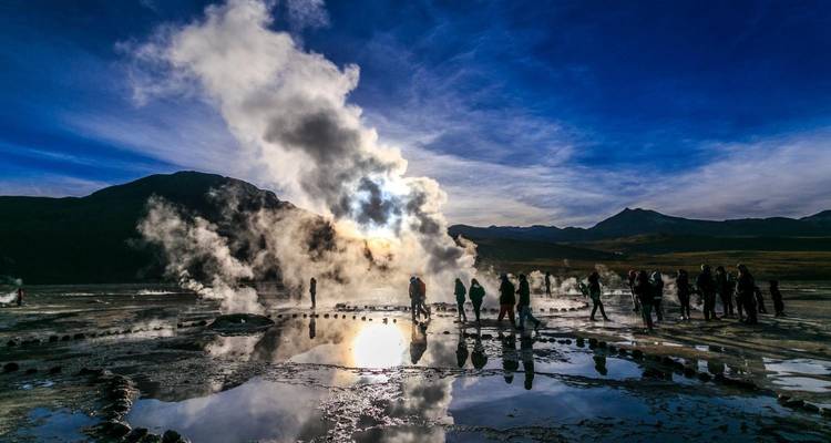 Grupo de turistas observando géiseres con vapor elevándose.