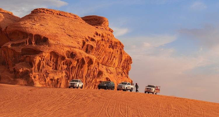 Des voitures garées près de formations rocheuses rouges dans un paysage désertique.