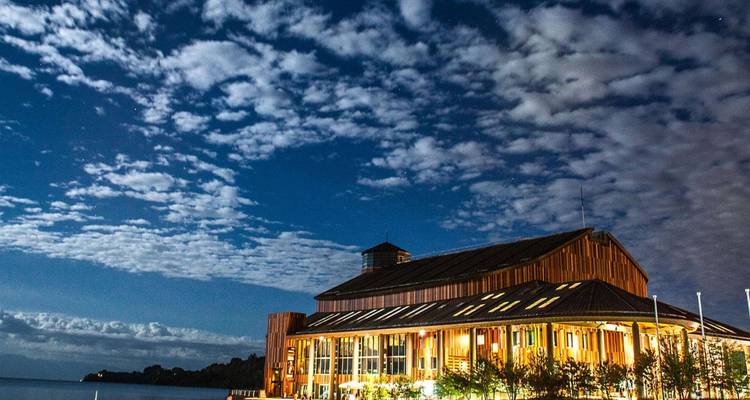 Bâtiment au bord du lac illuminé la nuit avec un ciel nuageux.
