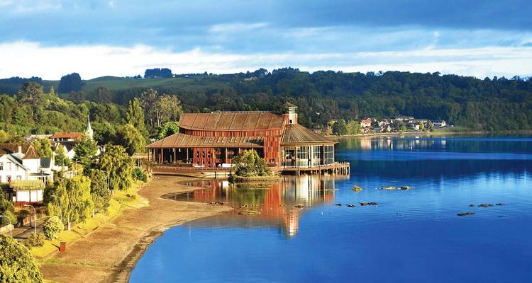 Bâtiment au bord du lac avec des collines boisées en arrière-plan.