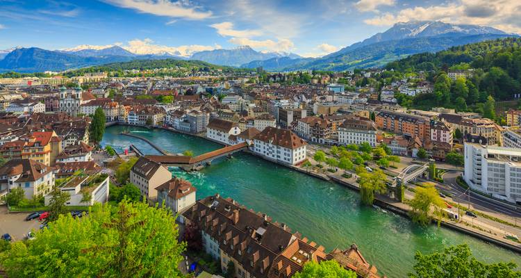 Aerial view of Lucerne’s old town, river and surrounding Swiss Alps under blue sky.