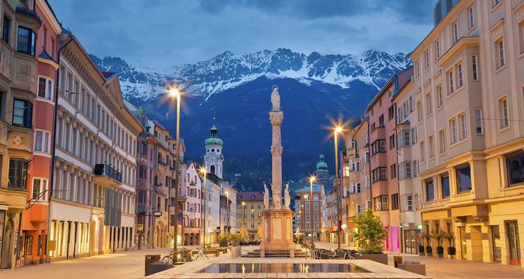 Evening lights along Innsbruck’s colorful street with Alps towering in the background.
