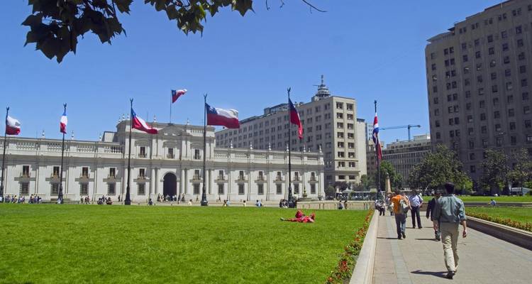 Edificio gubernamental en una plaza con banderas y personas paseando.