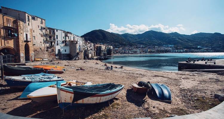 Pueblo costero con botes en una playa de arena y montañas al fondo.