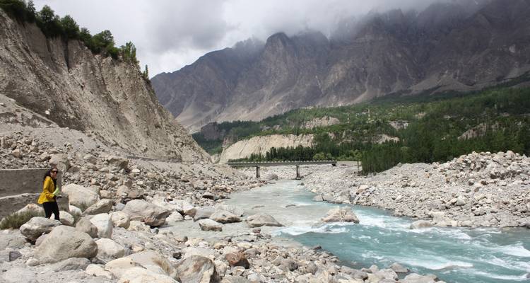Person, die auf Felsen an einem Fluss mit Bergen sitzt.