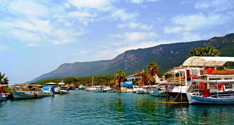 Scène de port avec des bateaux et des montagnes en arrière-plan.
