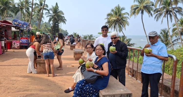 Group of people enjoying coconuts at a coastal promenade with palm trees.