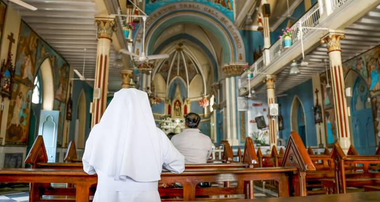 Interior of a church with people sitting on wooden benches and intricate architectural details.