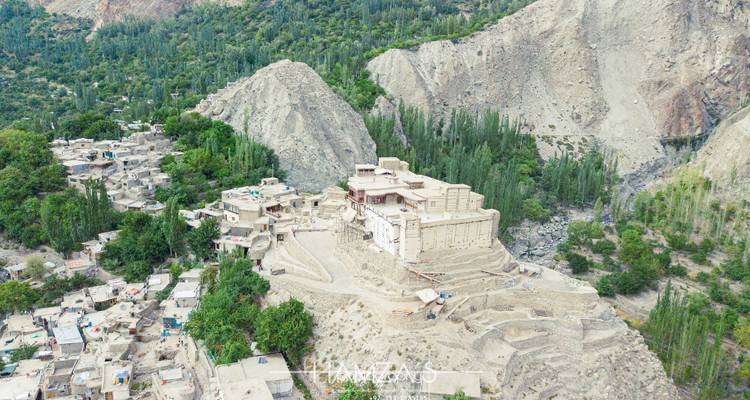 Luchtfoto van het historische Baltit Fort dat op een rotsachtige heuvel ligt, omgeven door dorpen in het Hunza Valley en steile bergen.