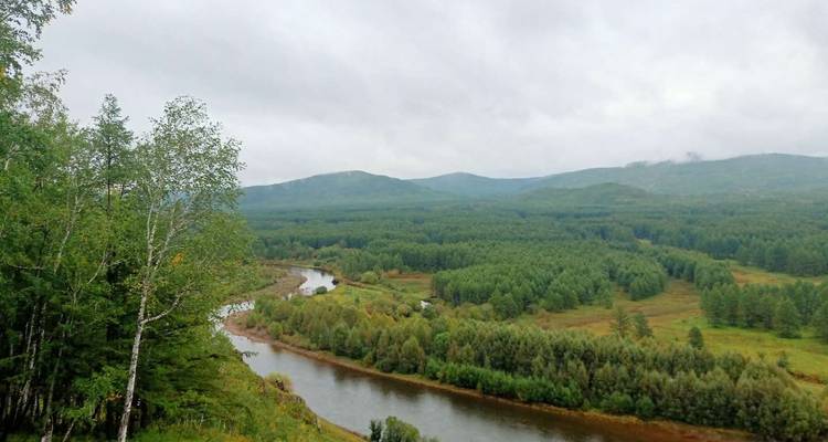 Fluss, der sich durch eine bewaldete Landschaft in Hailar, China, schlängelt.