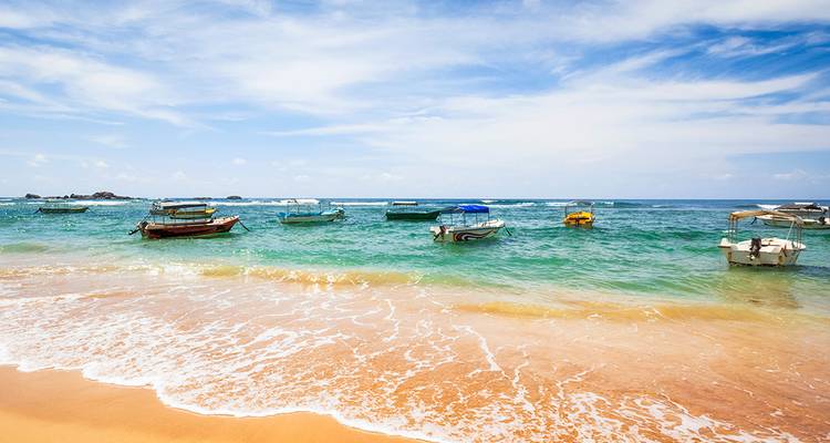 Playa tropical soleada con agua cristalina y coloridas barcas de pesca en el mar.