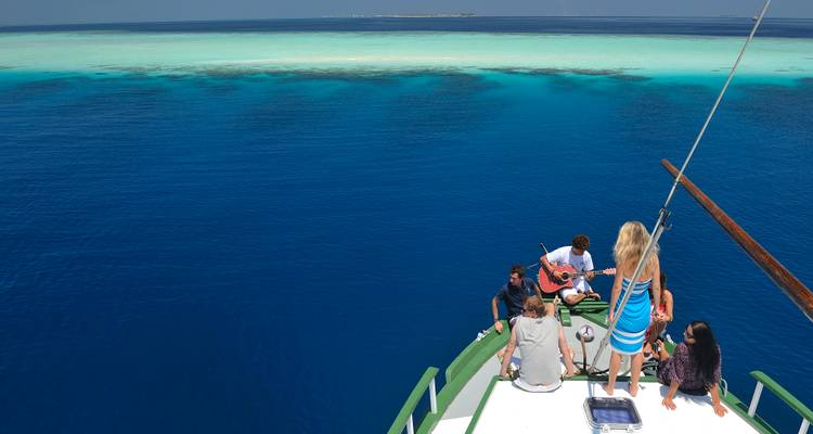 Grupo de viajeros en la proa de un barco sobre las aguas vividas y azules de los arrecifes de Maldivas.