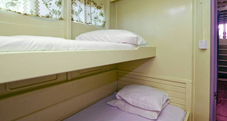 Cabine compacte avec des lits superposés jaune pâle soigneusement préparés avec des oreillers blancs à l'intérieur d'un bateau.