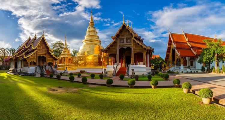 Goldene Pagode und traditionelle thailändische Gebäude in üppigen Gärten.
