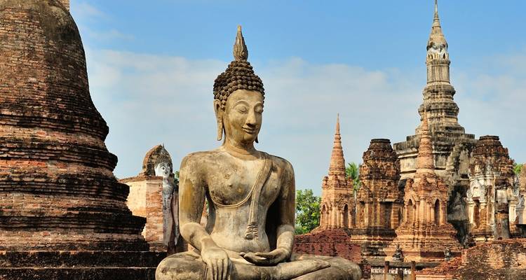 Ancient stone Buddha statue sits serenely among crumbling brick pagodas in a historical park.