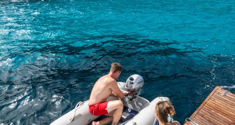 A person operating a small boat on clear blue water.