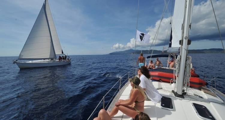 Menschen auf einem Segelboot genießen das Meer und die Sonne mit einem anderen Segelboot im Hintergrund.