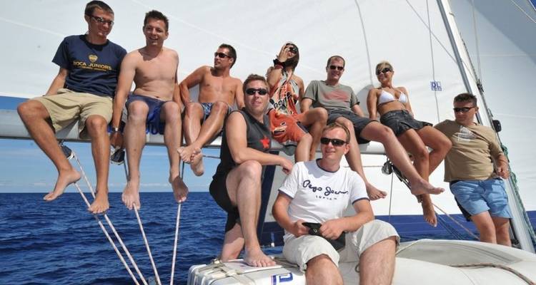 Acht Personen sitzen auf der Reling eines Segelboots und genießen die Aussicht.