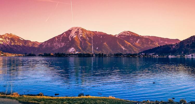 Un coucher de soleil éclatant au-dessus d'un lac de montagne avec des gens assis sur la rive.