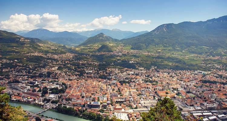 Elevated view of Trento with Adige River curving beside terracotta rooftops and layered mountain backdrop.