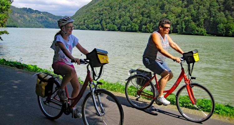 Zwei Personen fahren Fahrrad an einem Fluss mit üppig grüner Umgebung.
