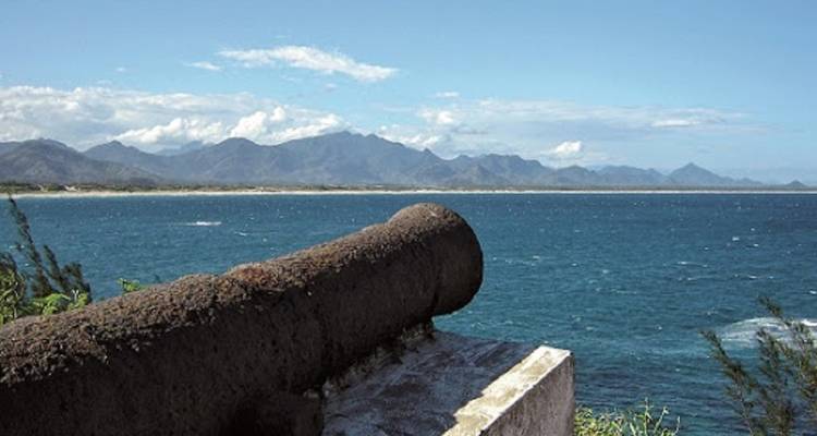 Oud kanon met uitzicht over de oceaan met bergen op de achtergrond.