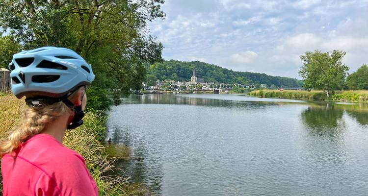 Un cycliste contemple un calme affluent de la Loire en direction d'un pittoresque village français niché dans des collines verdoyantes.