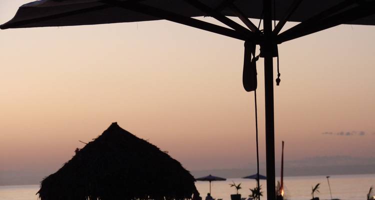 Silhouette eines Sonnenschirms und einer Hütte bei Sonnenuntergang.