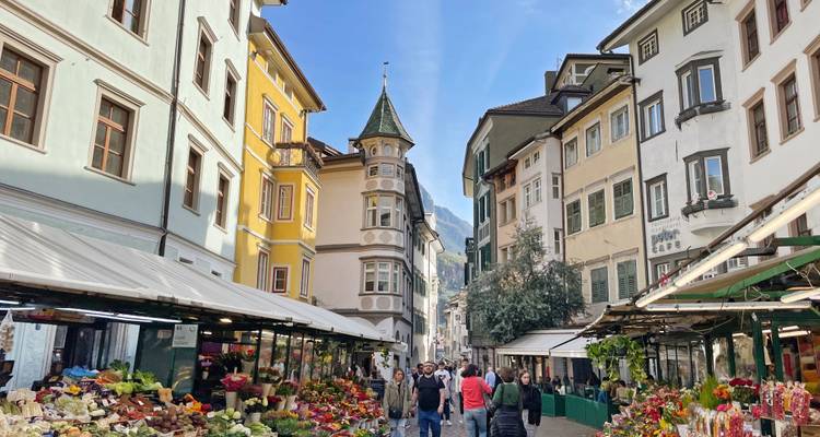 Drukke groentemarktkraam in de oude binnenstad van Bolzano omzoomd door kleurrijke gevels.