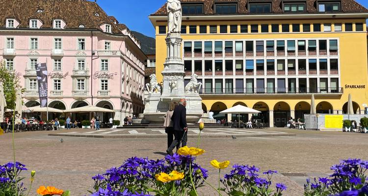 Centraal plein van Bolzano met het Walther-monument omringd door pastelkleurige gebouwen en verse bloemen.