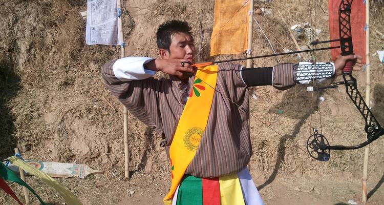 Een man in traditionele Bhutanese kleding die een pijl en boog richt.