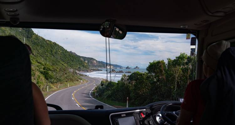 Vista a través del parabrisas de un autobús turístico de una carretera costera sinuosa y una costa accidentada.