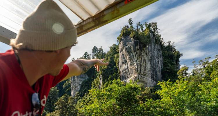 Un guía con gorro de lana señala hacia un acantilado de piedra caliza que se eleva desde la densa selva tropical.