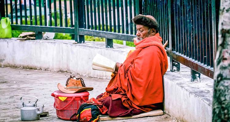 Mönch in roter Robe sitzt und liest an einem Zaun.